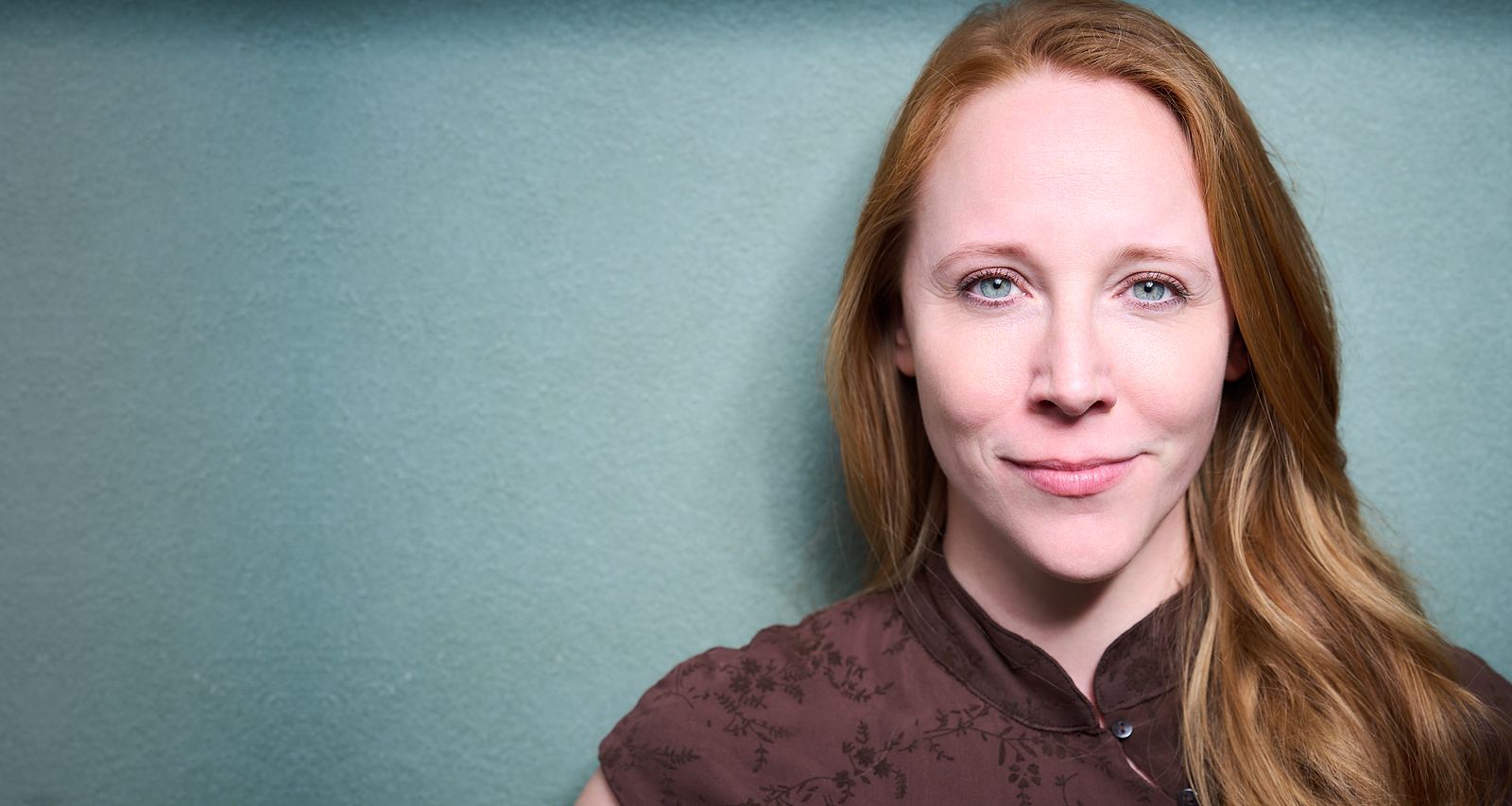 Debora Mergler, Trainerin für arbeitsnahe Kommunikation, lächelt vor einer ruhigen petrolgrauen Wand