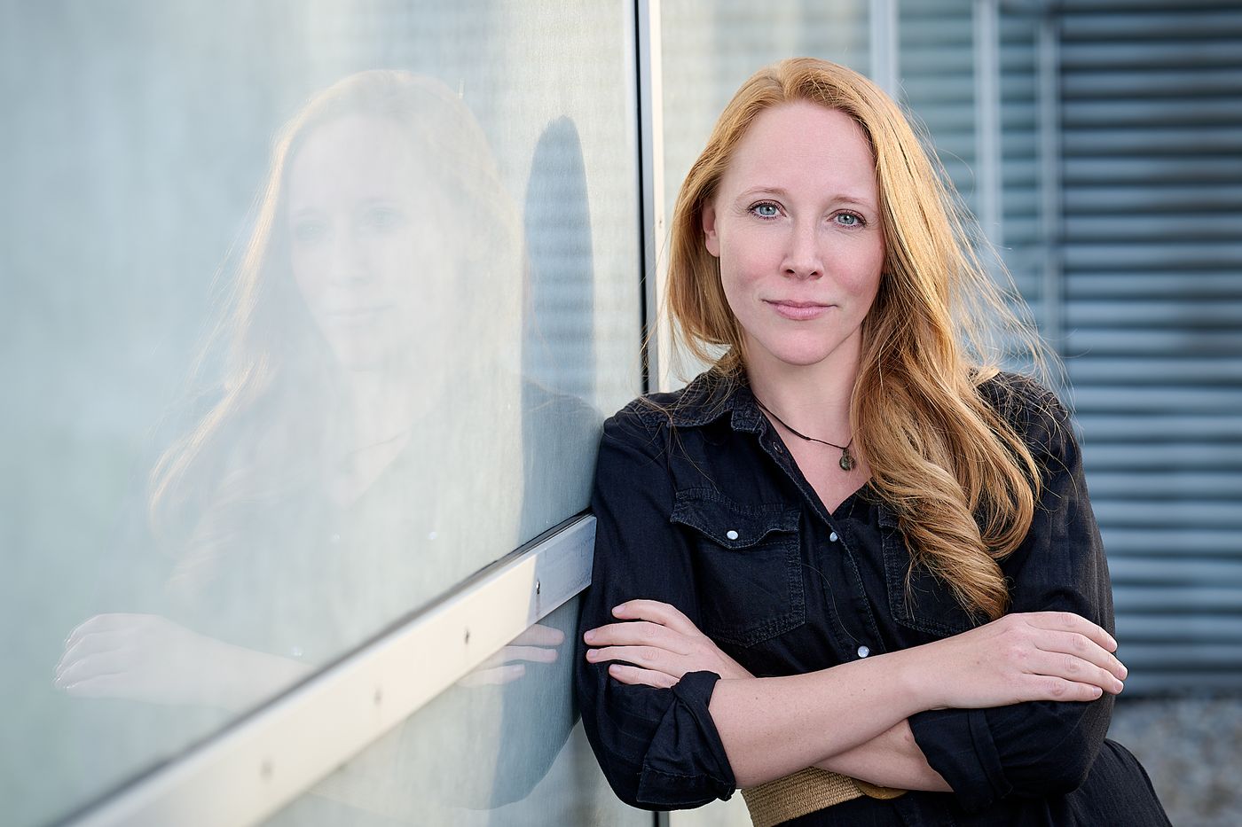 Debora Mergler lehnt mit verschränkten Armen an einer Glasfassade
